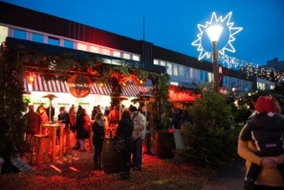 Weihnachtsmarkt Tibarg Blick auf einen beleuchteten Weihnachtsmarktstand mit Tannenzweigen-Dekoration